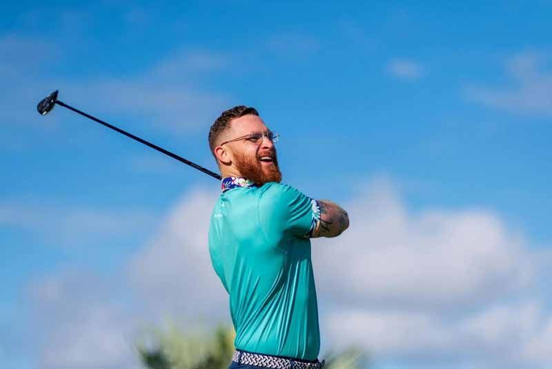 Golfer in teal shirt mid-swing against a bright blue sky