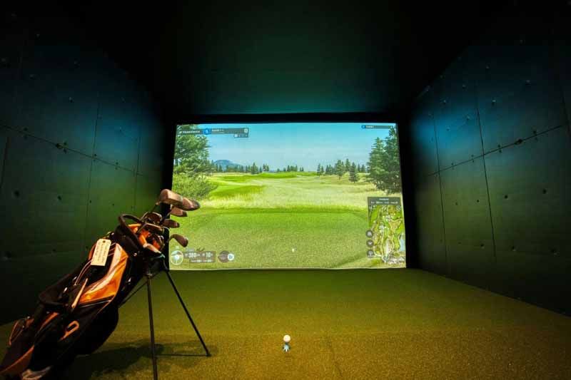 Indoor golf simulator with a golf bag in the foreground and a course projected on a screen.