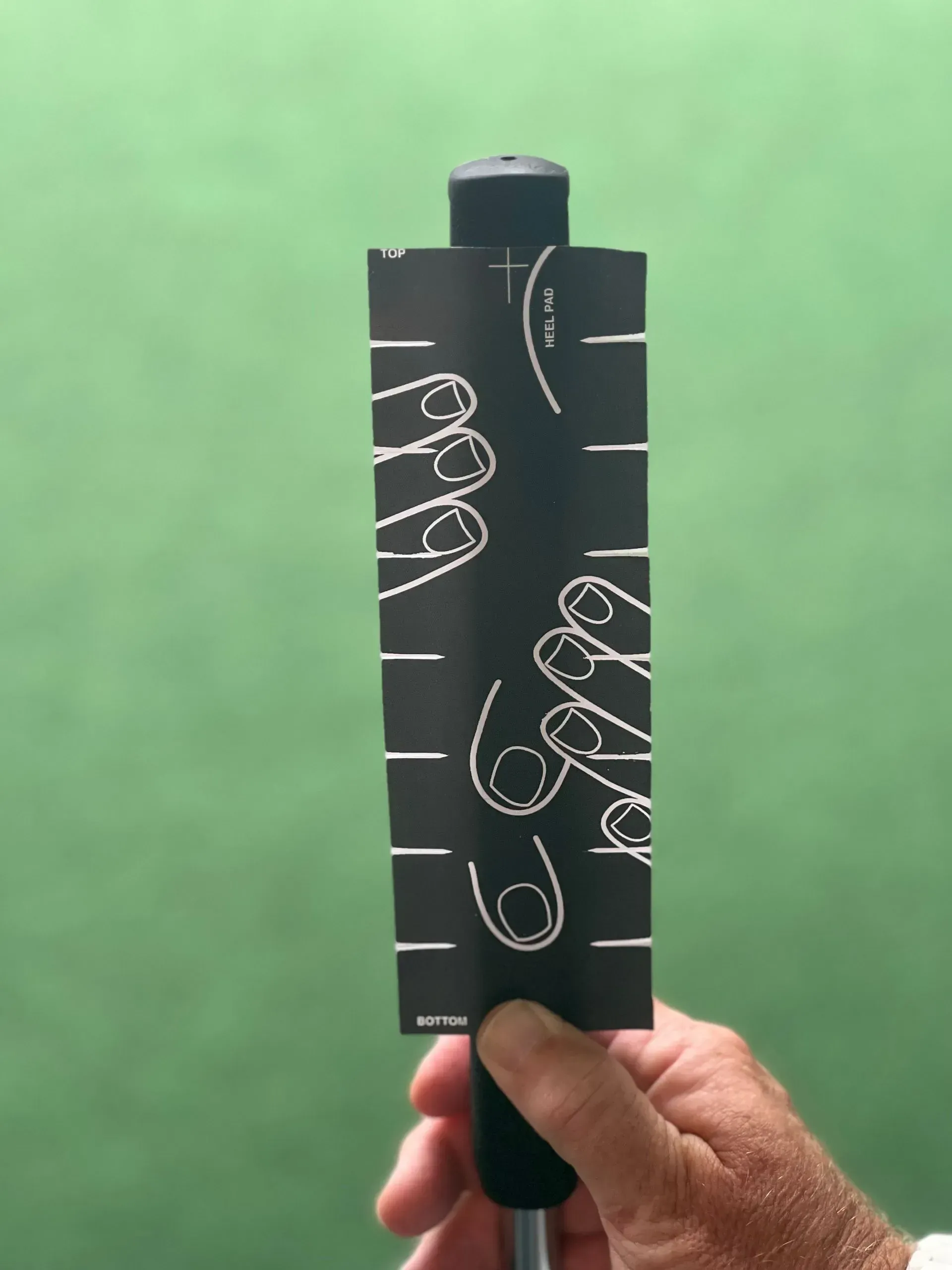 Hand holding a black measuring card with white markings against a blurred green background
