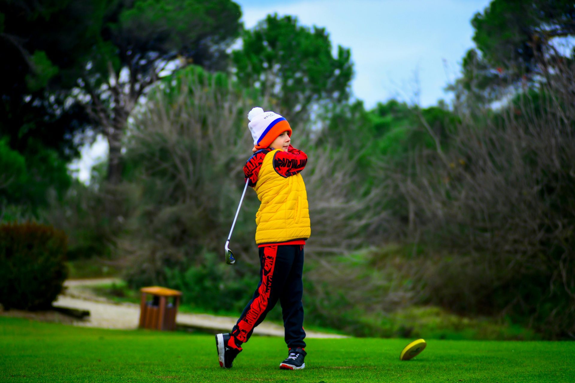 Golfer in yellow jacket and red pants swinging on a green course