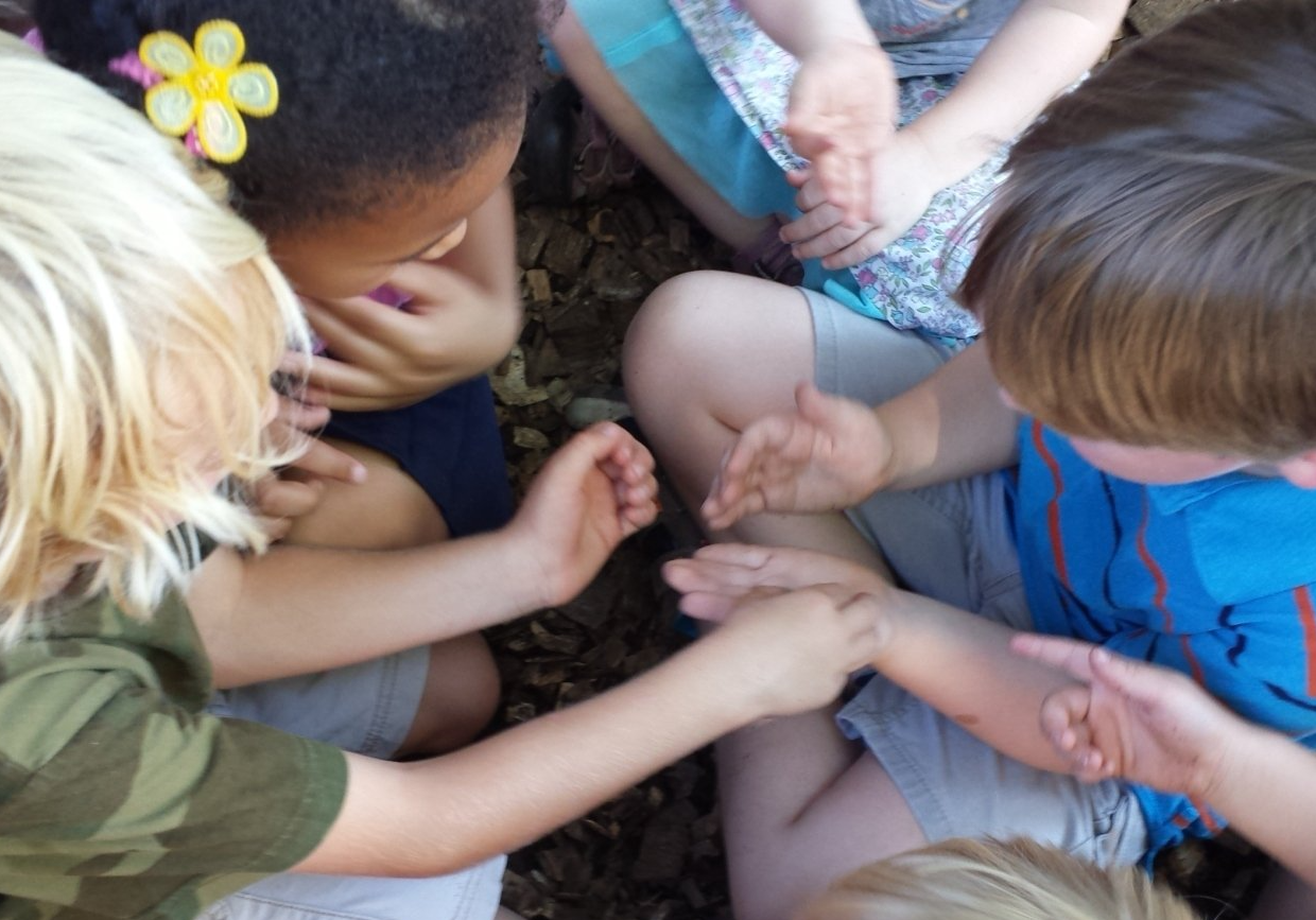 A group of children siting on the ground playing with their hands