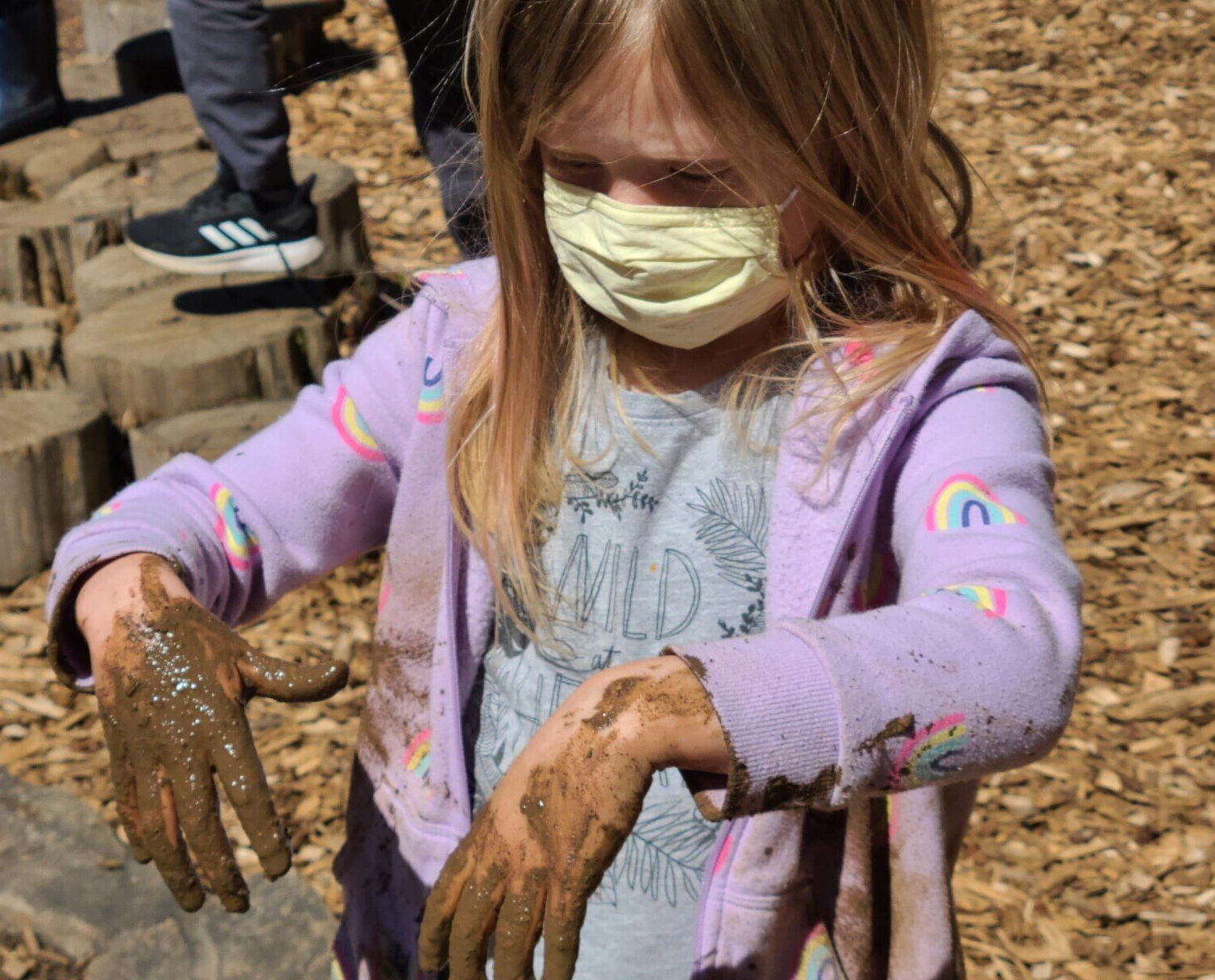 A little girl wearing a mask is playing in the mud.