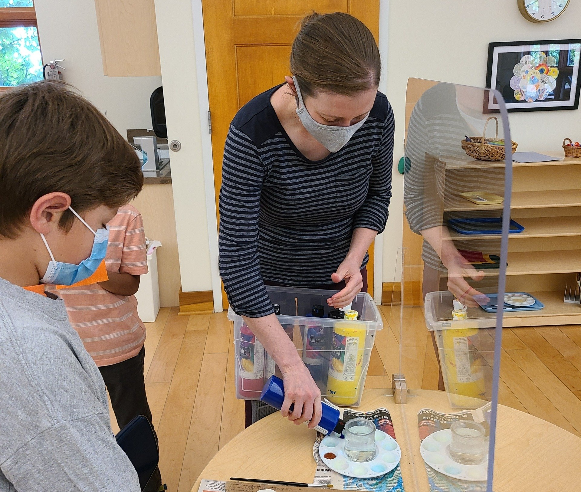 A montessori guide wearing a mask is standing next to a boy wearing a mask