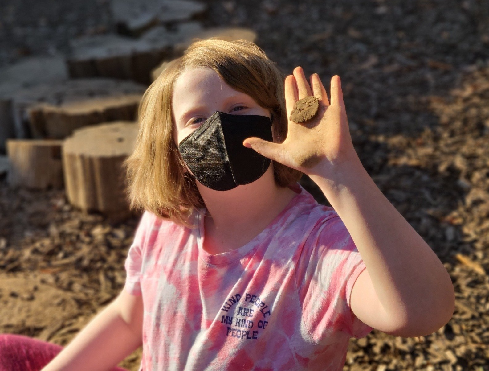 A young girl wearing a face mask is holding a rock in her hand.