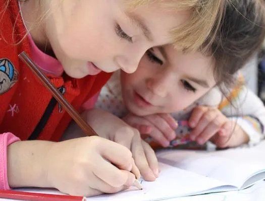 Two little girls are sitting at a table writing in a notebook.