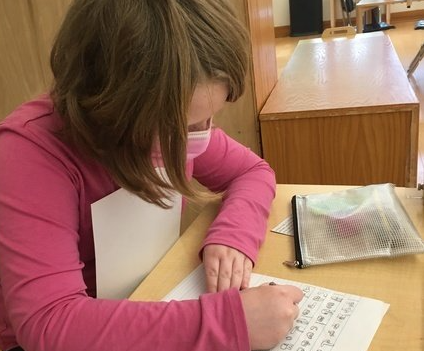 A young girl wearing a pink shirt is writing on a piece of paper.