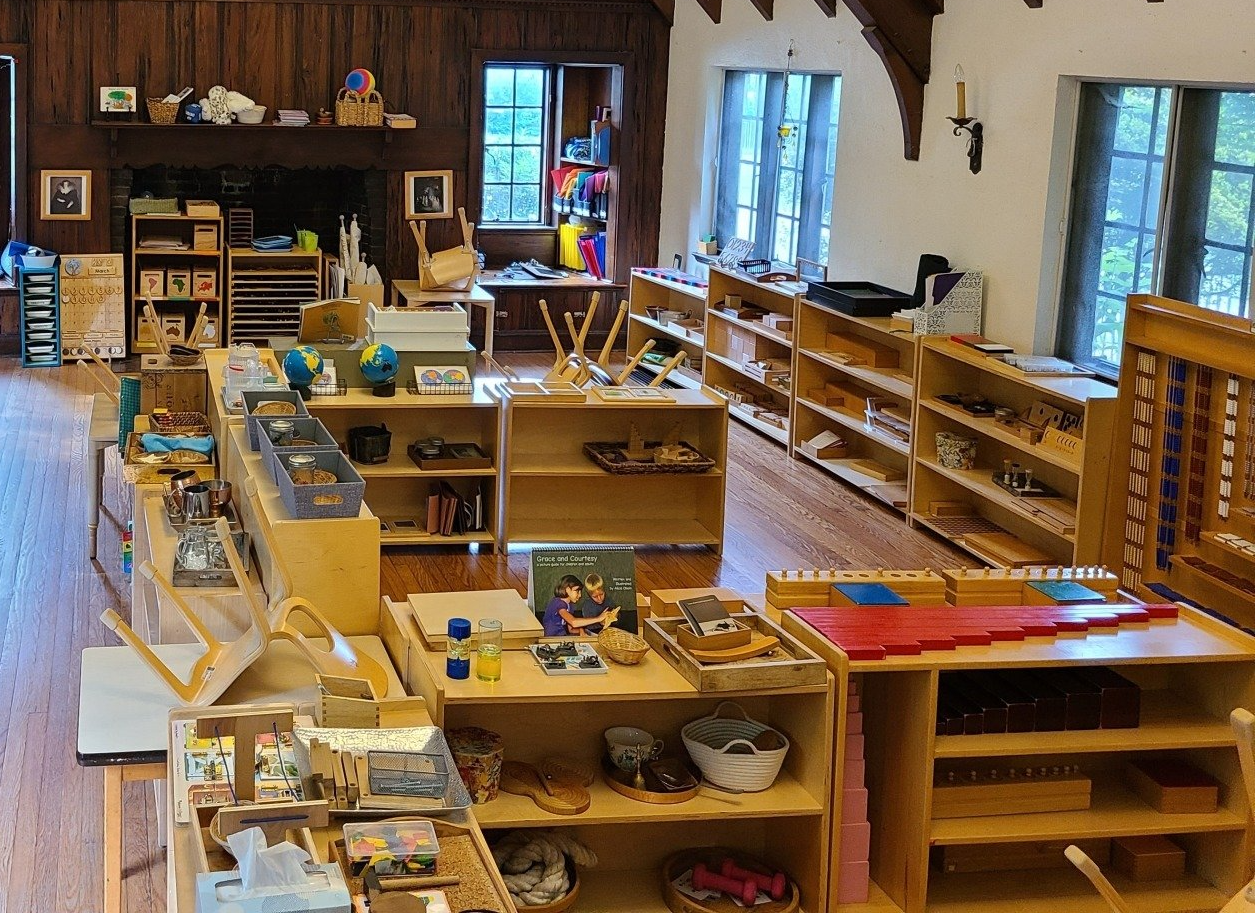 A large montessori classroom filled with wooden shelves, tables and montessori materials.