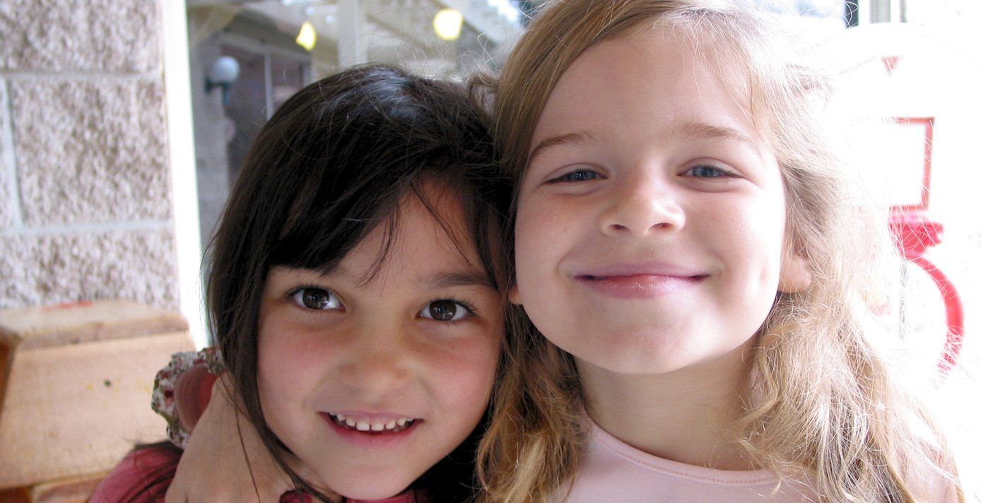 Two little girls are hugging each other and smiling for the camera.