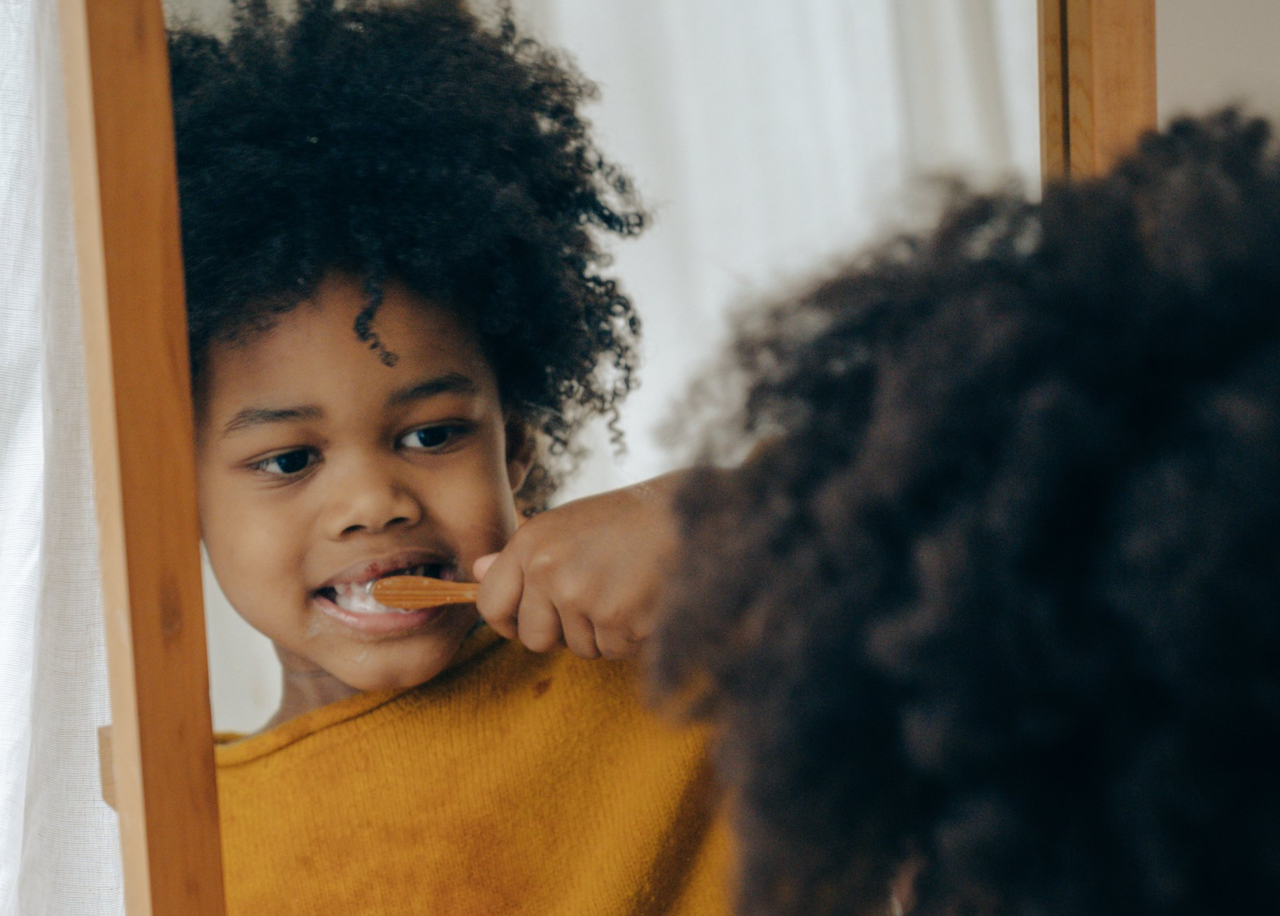 A young boy is brushing his teeth in front of a mirror.