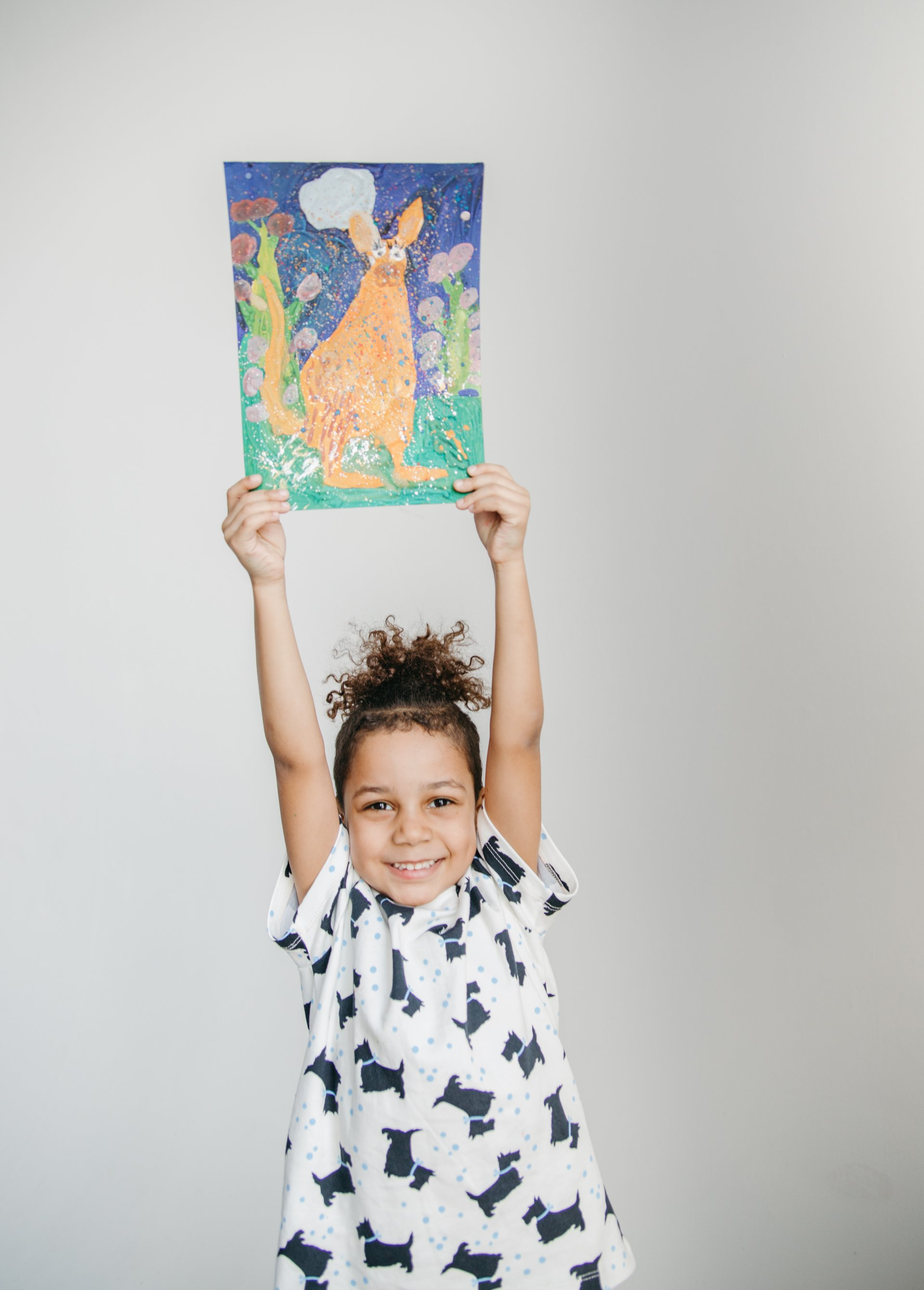 A little girl is holding up a painting of a kangaroo.