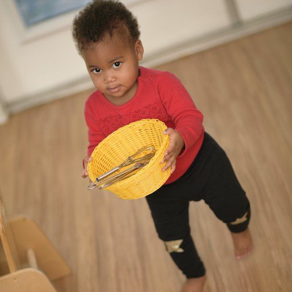 A toddler boy in a red shirt is holding a yellow basket.