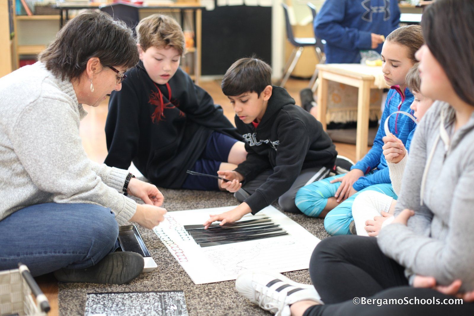 A group of children are sitting on the floor with a montessori guide.