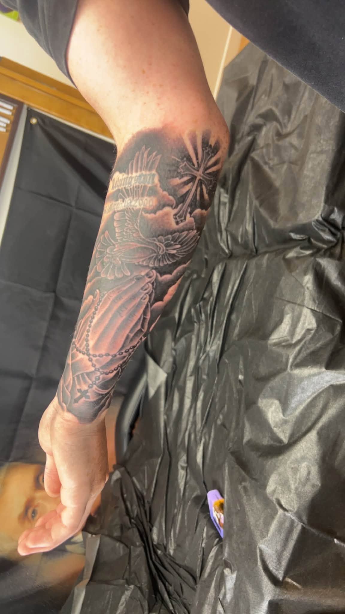 Forearm with a colorful floral tattoo sleeve resting on a black plastic-covered surface