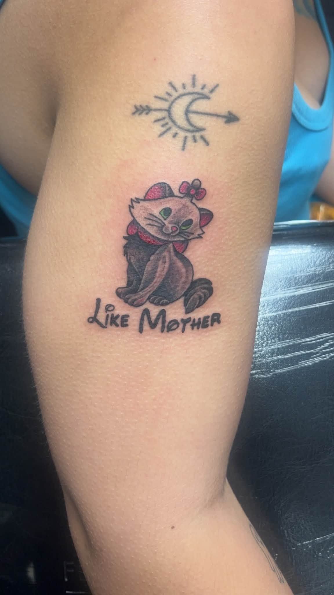 Arm with two tattoos: crescent moon and sun above, and a rose with “Like Mother” below