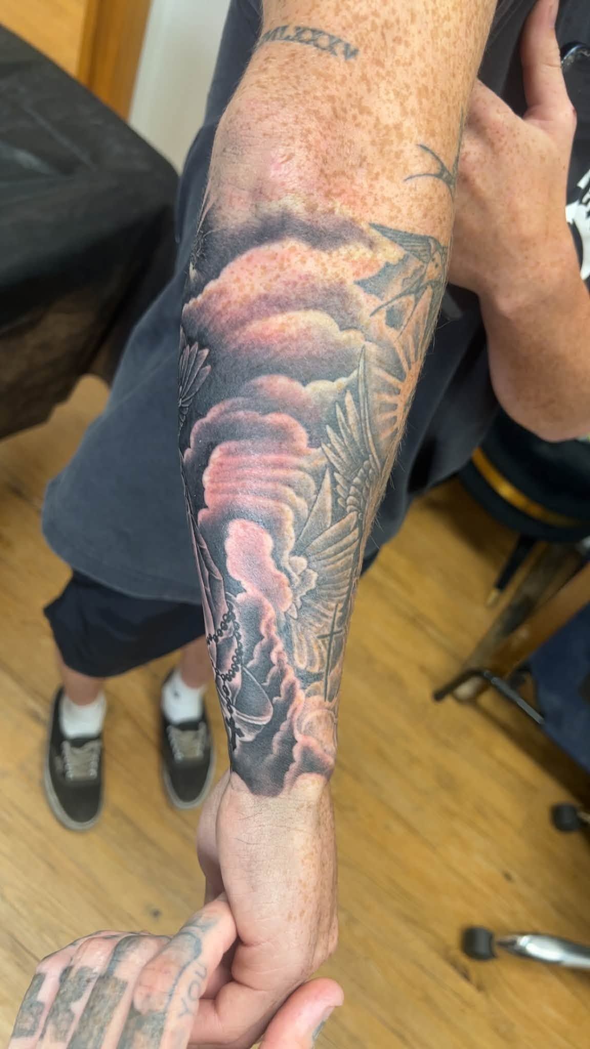 Tattooed forearm with a colorful sleeve tattoo featuring a stormy, tunnel-like scene.