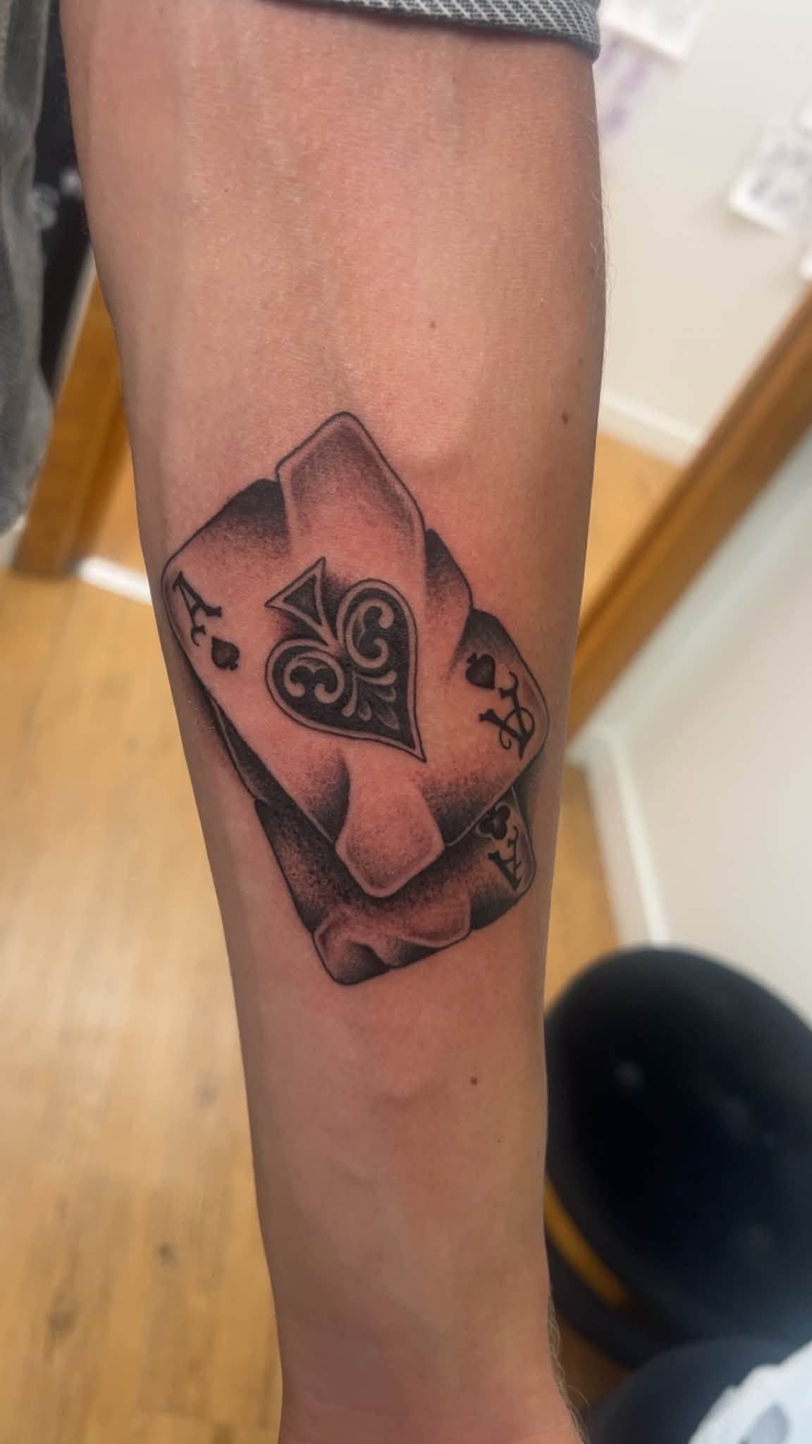 Close-up of a forearm with a black-and-red playing card tattoo, featuring a spade symbol and rose design