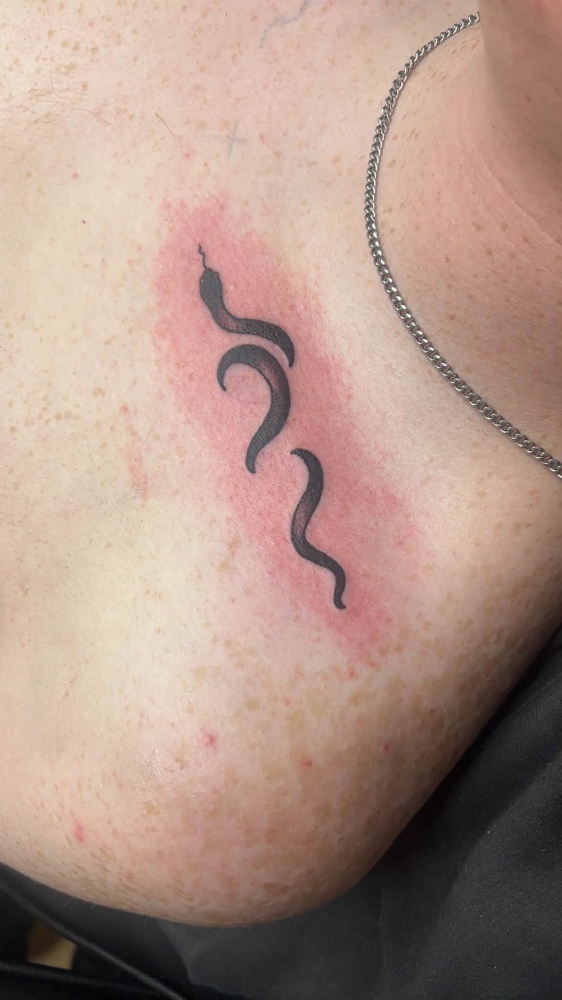 Close-up of a neck with a small black wavy tattoo on a pink-red irritated patch