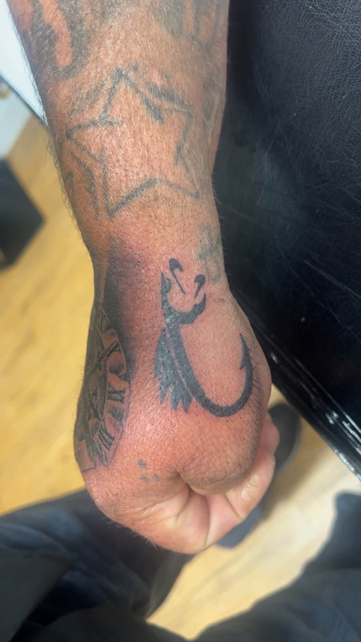 Close-up of a tattooed forearm and hand with black and gray tattoo designs on a wooden floor