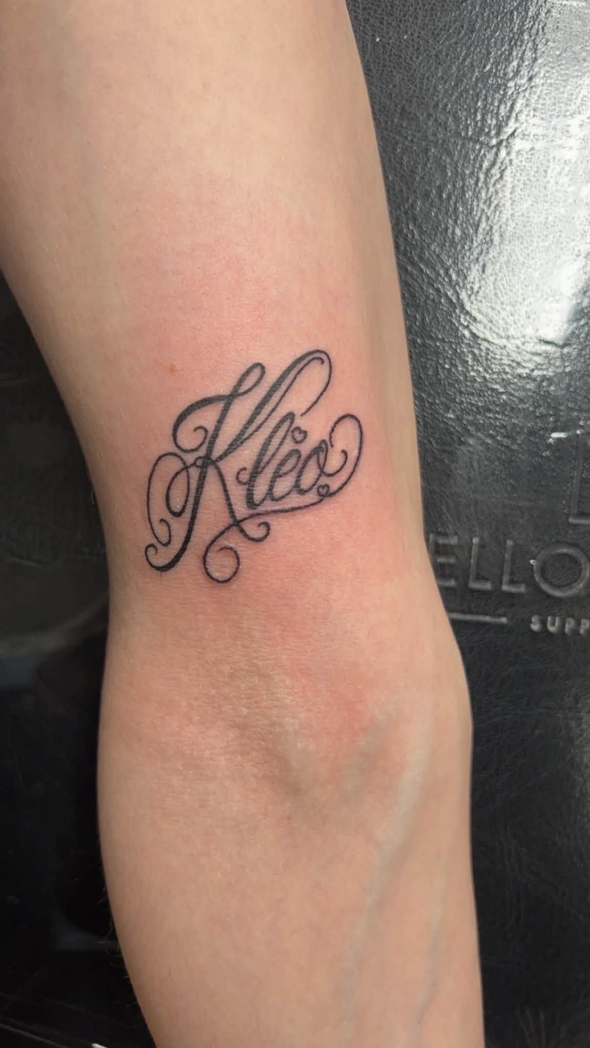Small black cursive tattoo on a forearm against a dark background