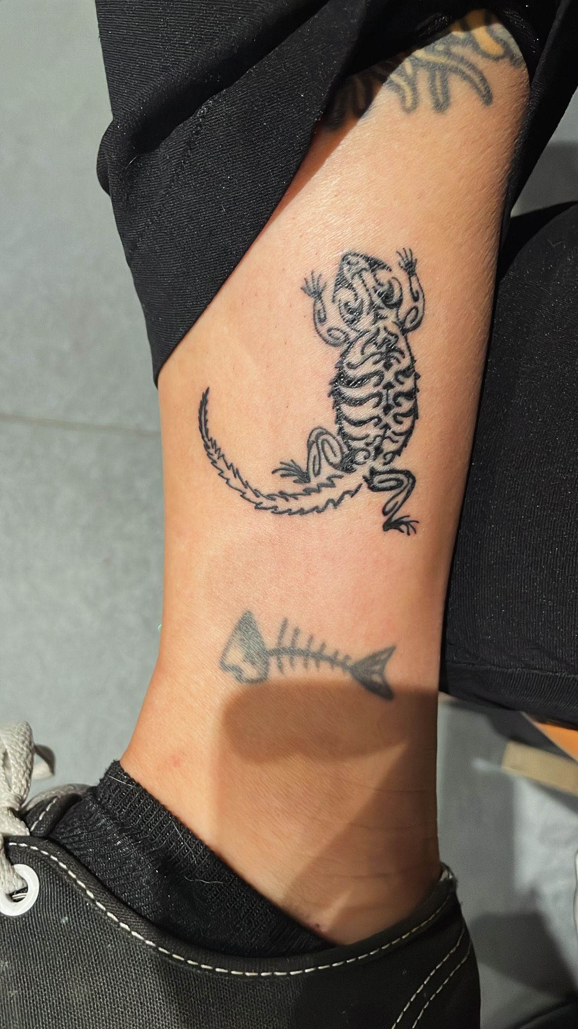 Close-up of a person’s ankle with a small black tattoo of a cartoon cat-like figure