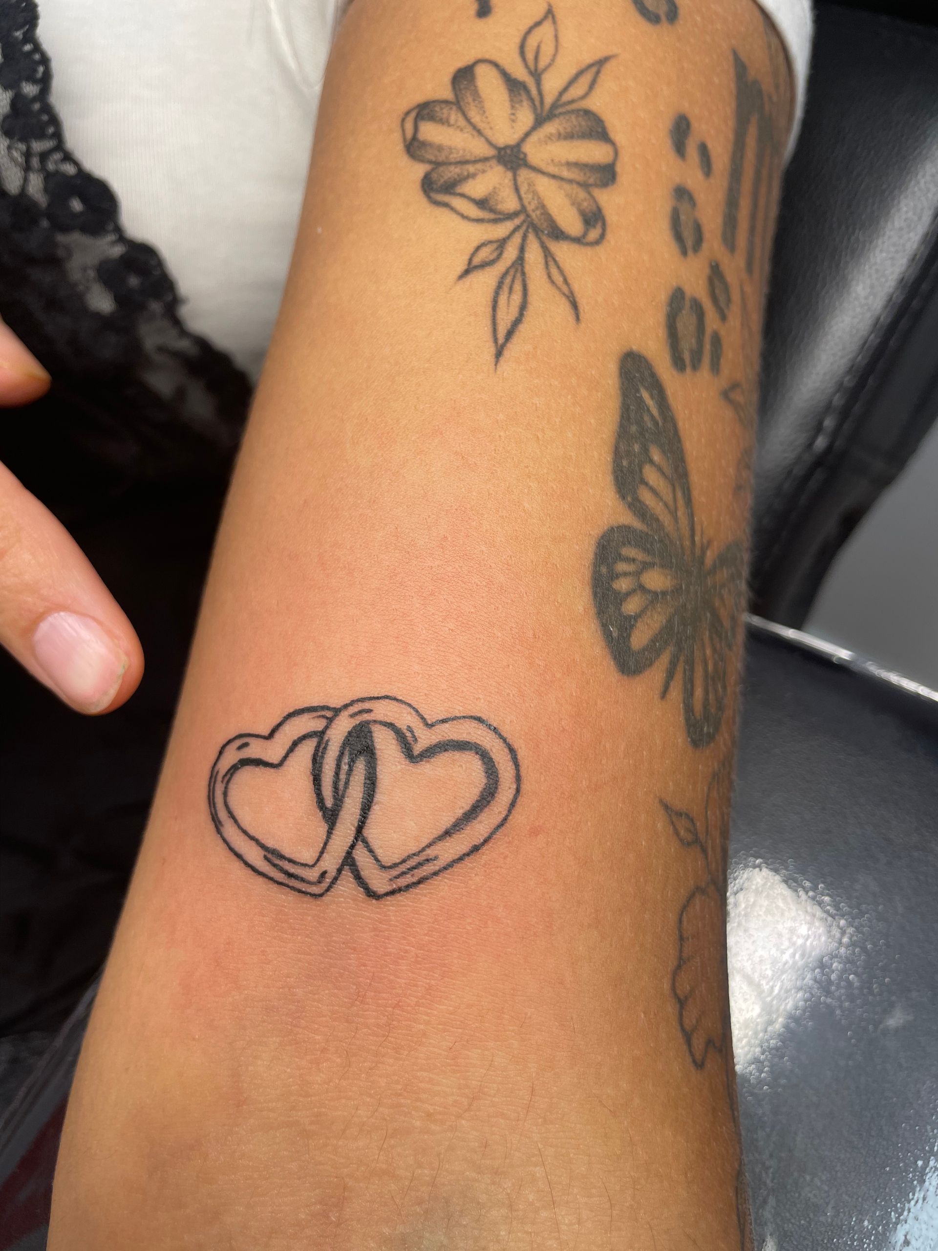 Forearm with several black tattoos, including a linked heart design and floral patterns