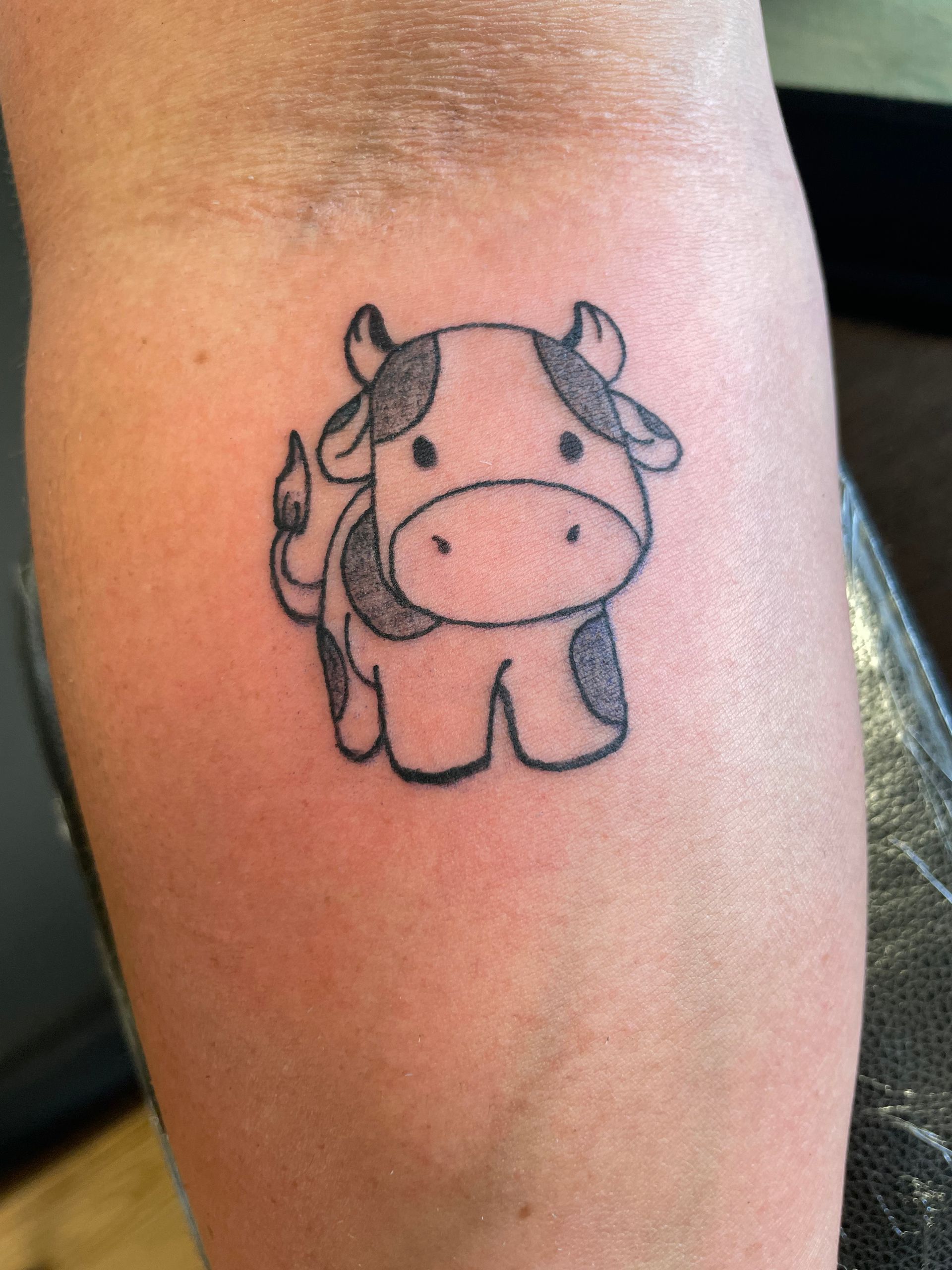 Small black cow tattoo on a person’s skin, with tiny horns and a simple cartoon style