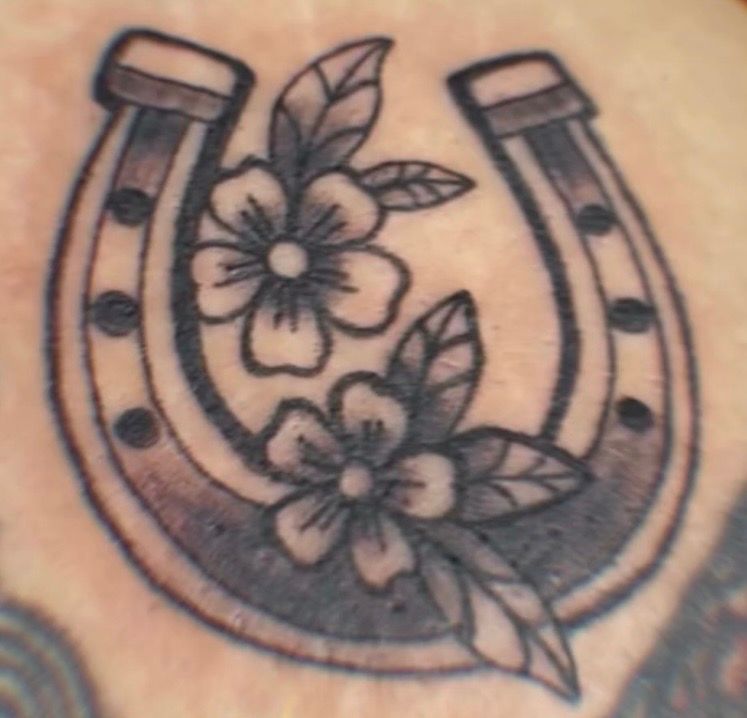 Black horseshoe tattoo with two flowers and leaves on skin