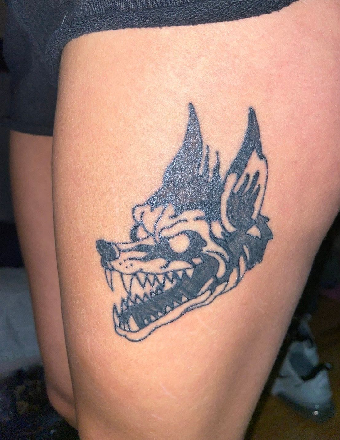 Black wolf head tattoo on a person’s calf, with pointed ears and bared teeth.