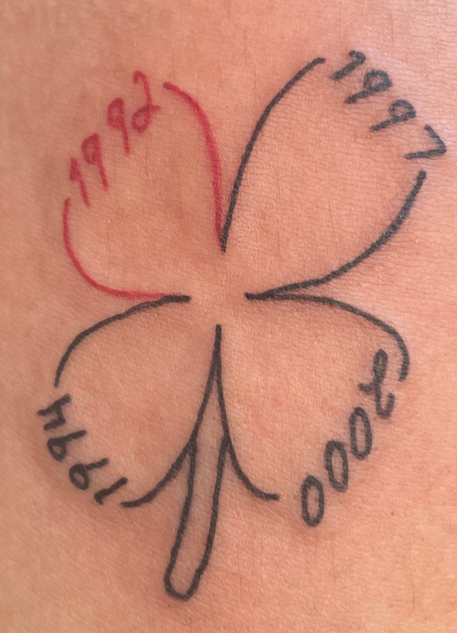 Four-leaf clover tattoo with handwritten dates in red and black ink