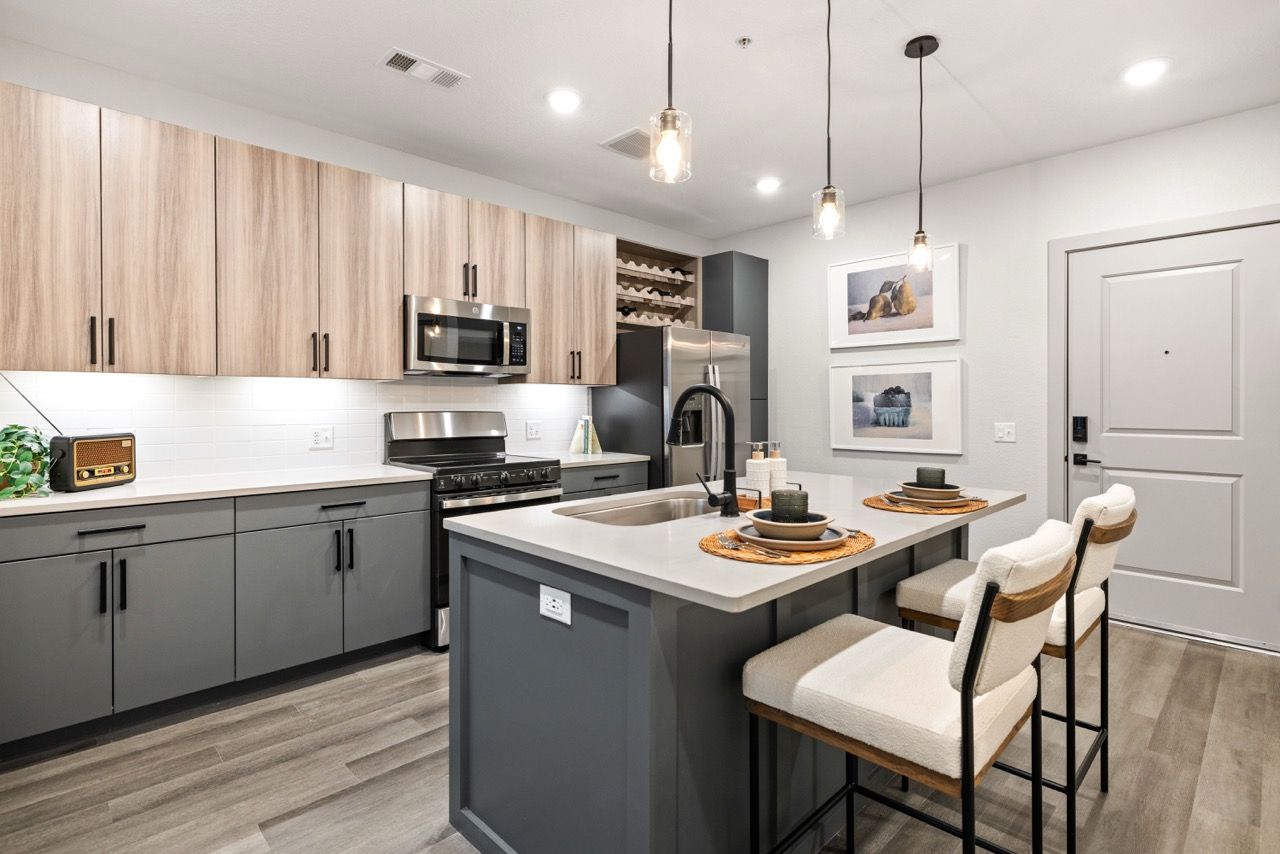 Modern apartment kitchen with an island, gray base cabinets, wood-tone upper cabinets, and stainless-steel appliances.
