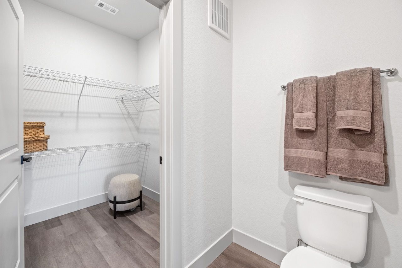 Walk-in closet with white wire shelving beside a bathroom toilet and towel rack.