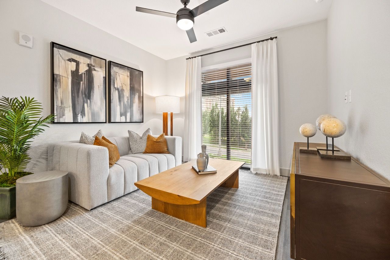 Living room with gray sofa, wooden coffee table, rug, and a large window with blinds.