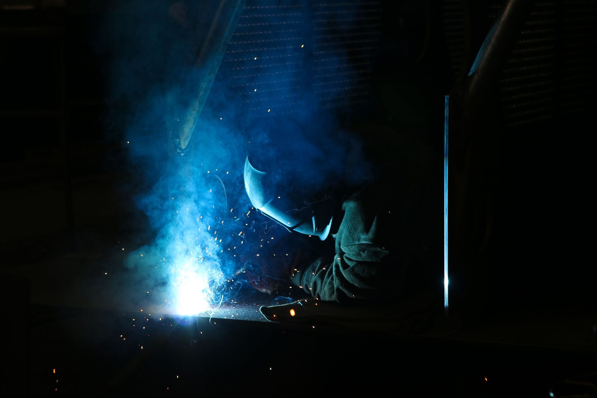 Worker welding a black metal railing on a staircase, with sparks flying outdoors