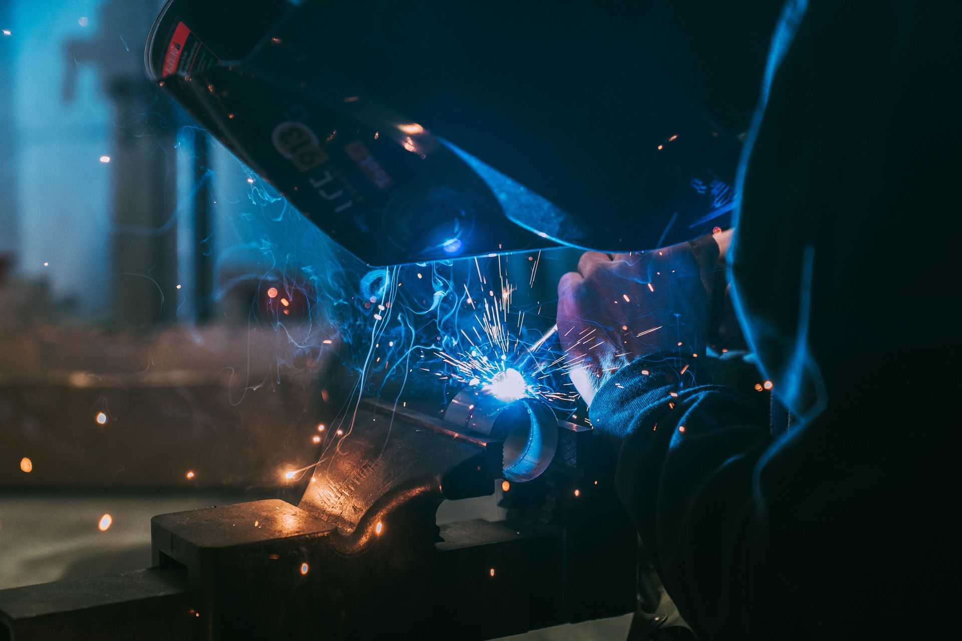 Welding sparks on metal rods held by a gloved hand, with bright arc light in a workshop.
