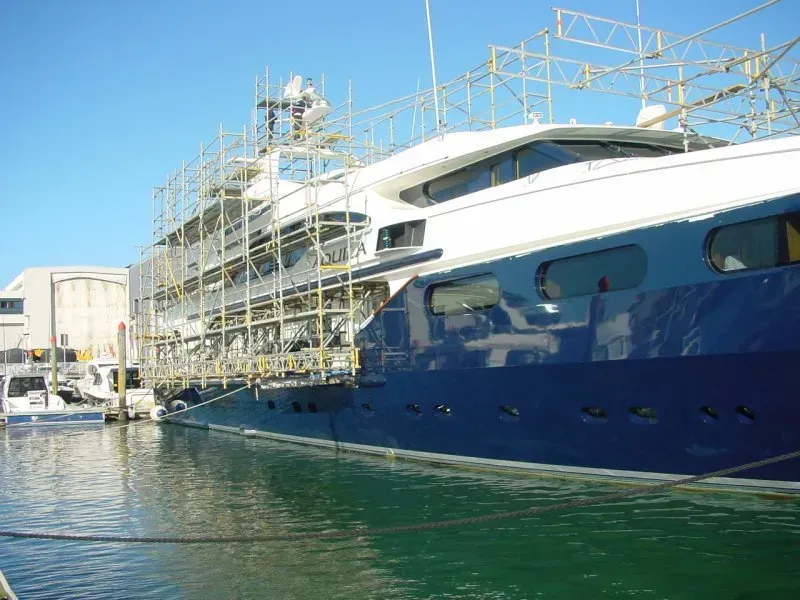 A large superyacht with significant scaffold on and suspended from it over the water