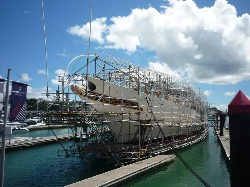 a scaffold structure over a boat prior to shrink wrap encapsulation suspended from the boat on the water