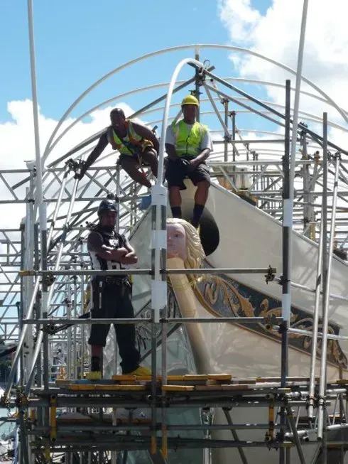 A group of construction workers standing on top of a scaffolding structure over a boat on the water