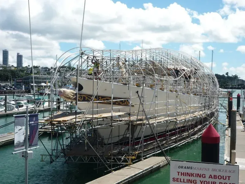 a scaffold structure over a boat prior to shrink wrap encapsulation suspended from the boat on the water