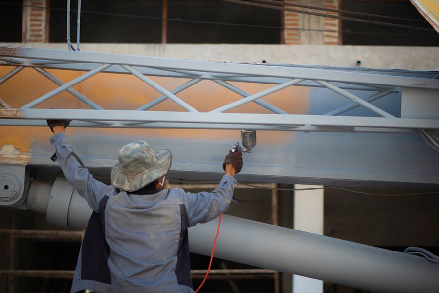 A Man Is Spray Painting a Metal Structure on A Construction Site — Alamo Powder Coaters in Unanderra, NSW
