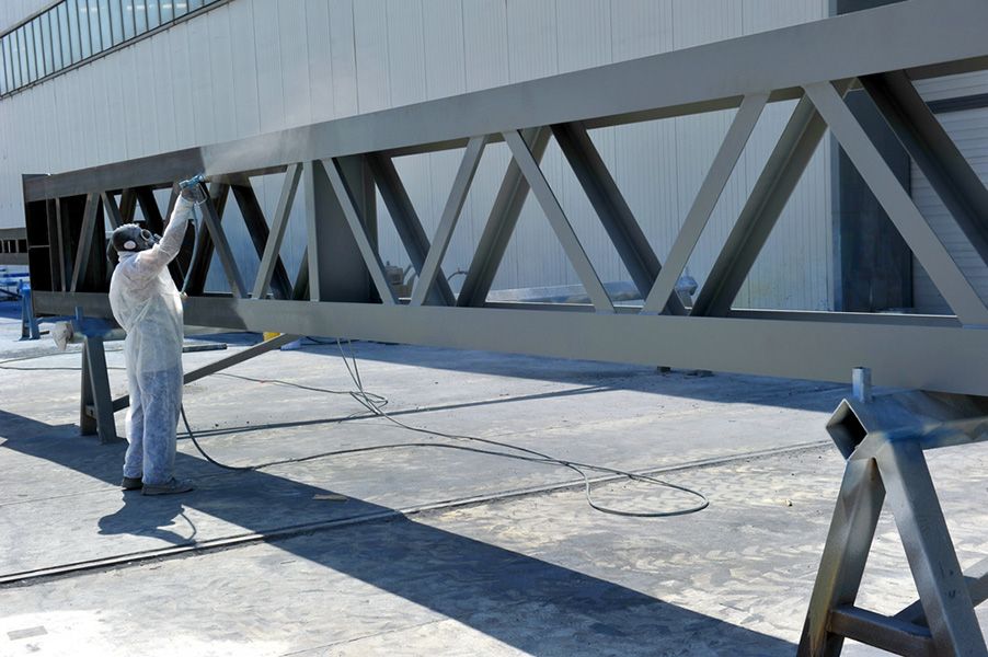 A Man Is Spray Painting a Metal Structure Outside of A Building — Alamo Powder Coaters in Unanderra, NSW