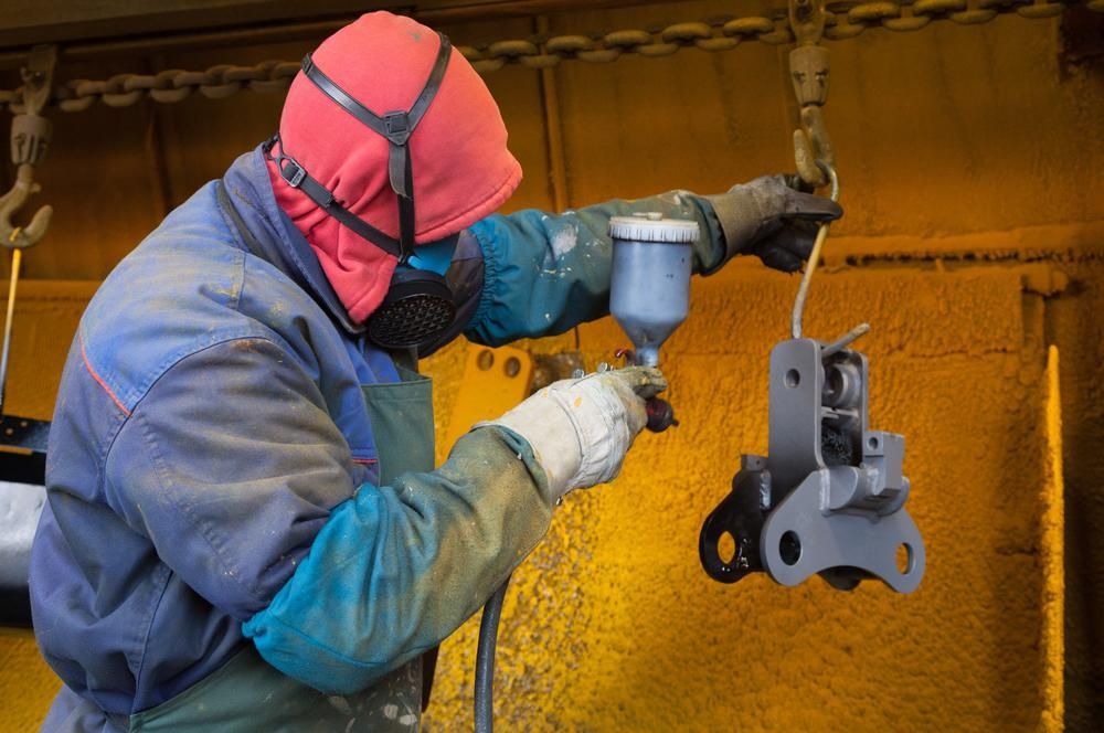 A Man Wearing a Mask is Spray Painting a Piece of Metal — Alamo Powder Coaters in Bowral, NSW