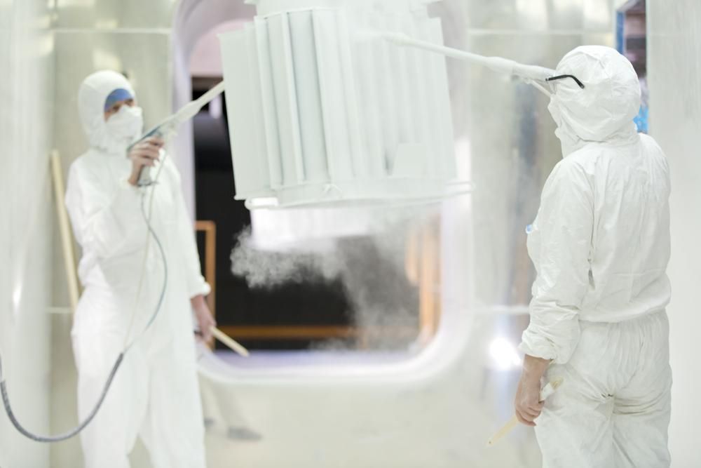 Two People in White Suits Are Spraying a White Object in a Room — Alamo Powder Coaters in Heathcote, NSW