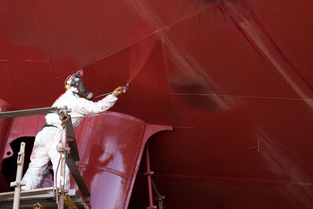 A Man in a White Suit is Painting a Red Boat — Alamo Powder Coaters in Nowra, NSW