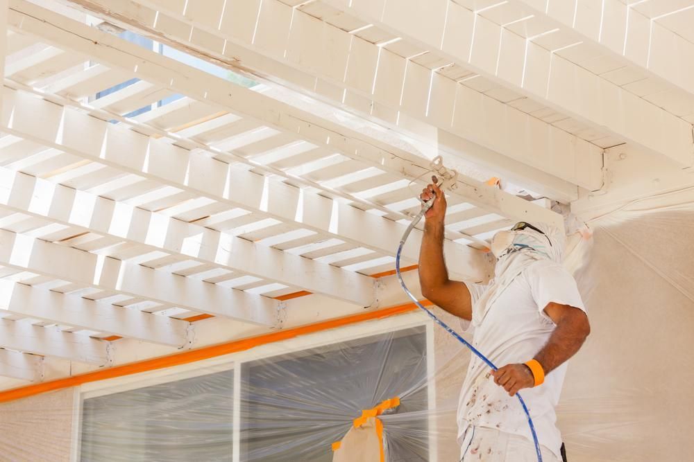 A Man is Spray Painting the Ceiling of a Building — Alamo Powder Coaters in Heathcote, NSW