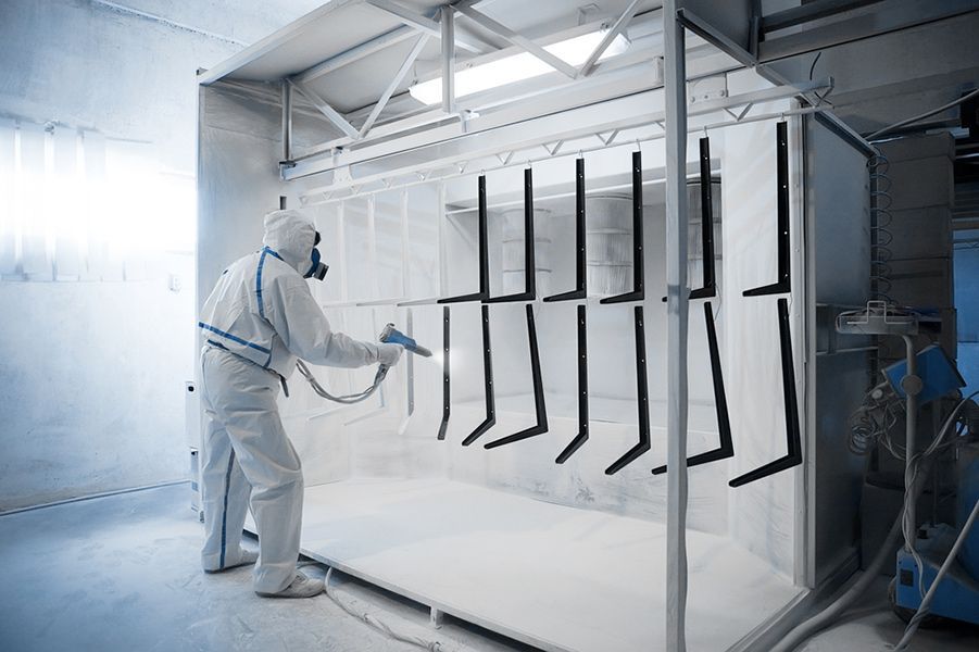 A Man Wearing a Protective Suit Spray Painting a Metal Object — Alamo Powder Coaters in Unanderra, NSW