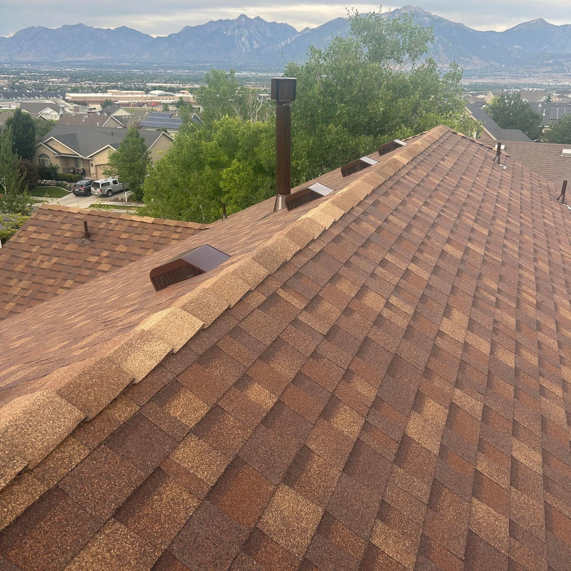 Brown shingle rooftop with chimney, overlooking a suburban valley and distant mountains under a hazy sky