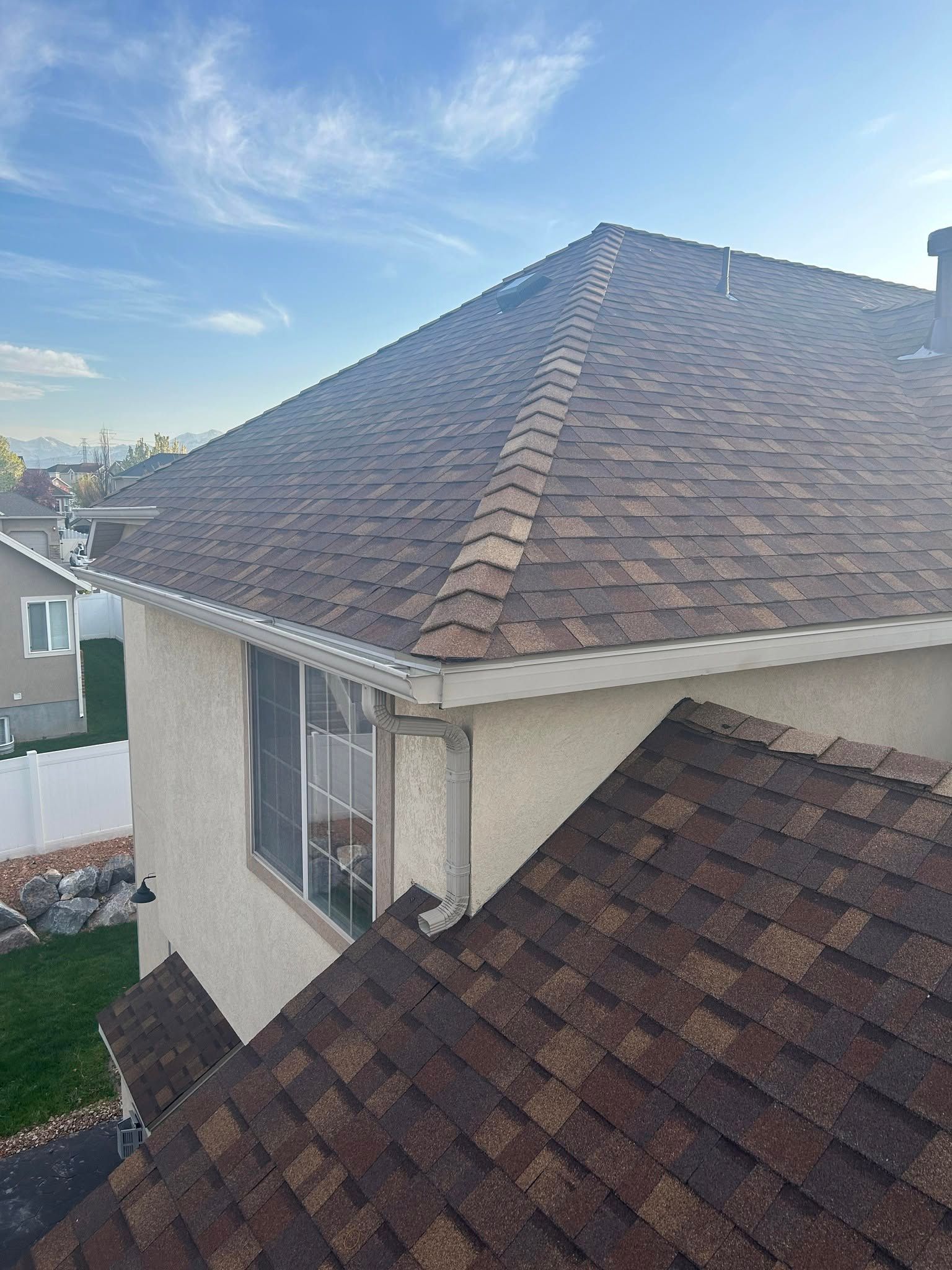Rooftop with brown shingles on a house under a blue sky, viewed from above.