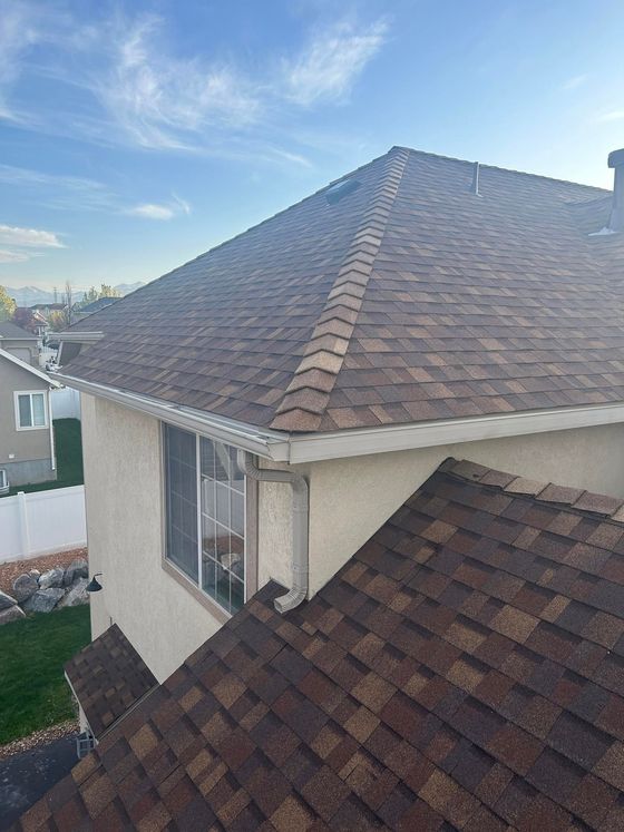 Rooftop with brown shingles on a house under a blue sky, viewed from above.