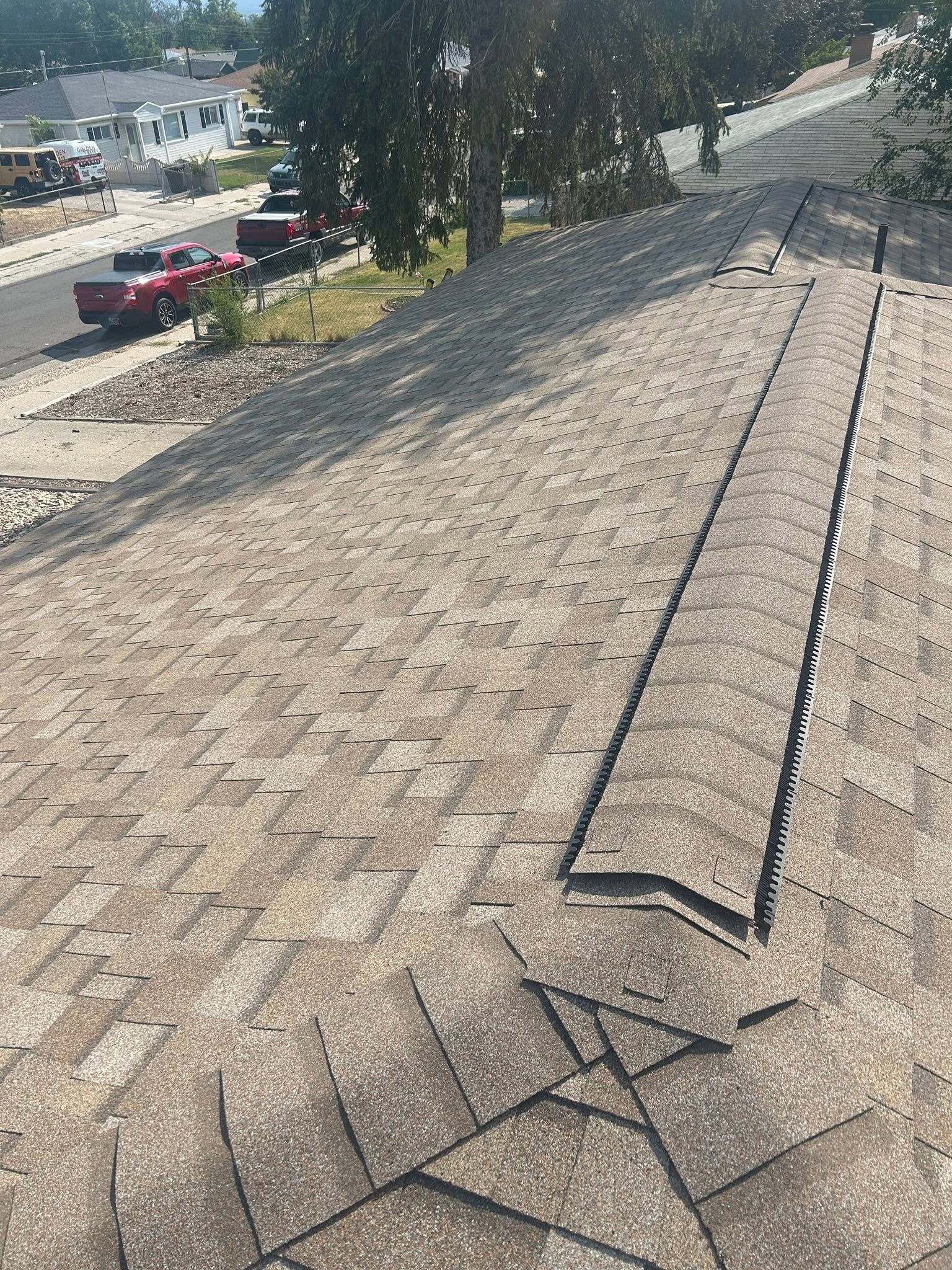 Roof shingles with visible damage and a long raised seam on a sunlit rooftop.