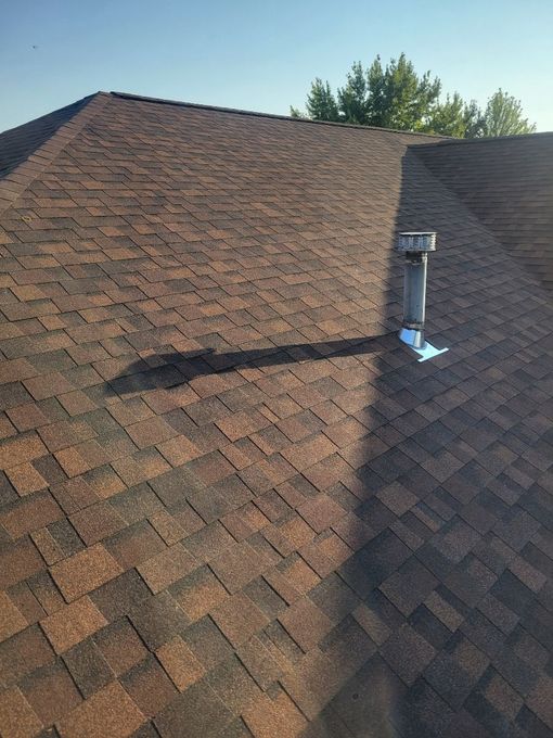 Brown shingle roof with a metal chimney vent and bright sunlight casting shadows